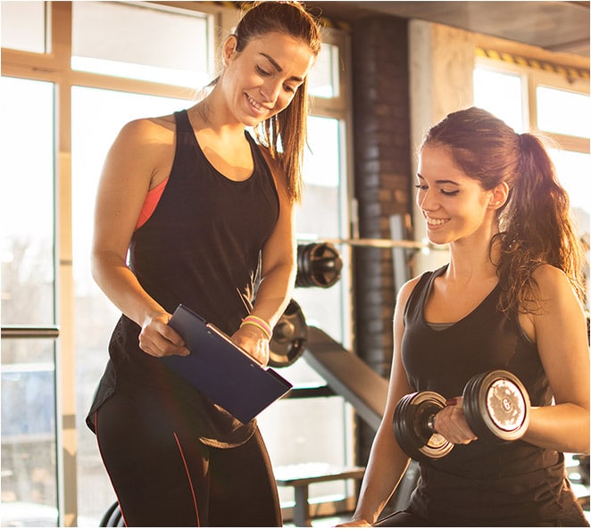 A Certified Personal Trainer shows her clipboard to a woman doing arm curls with a weight