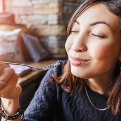 young asian woman sitting in a cafe and holding a fork looking pleased