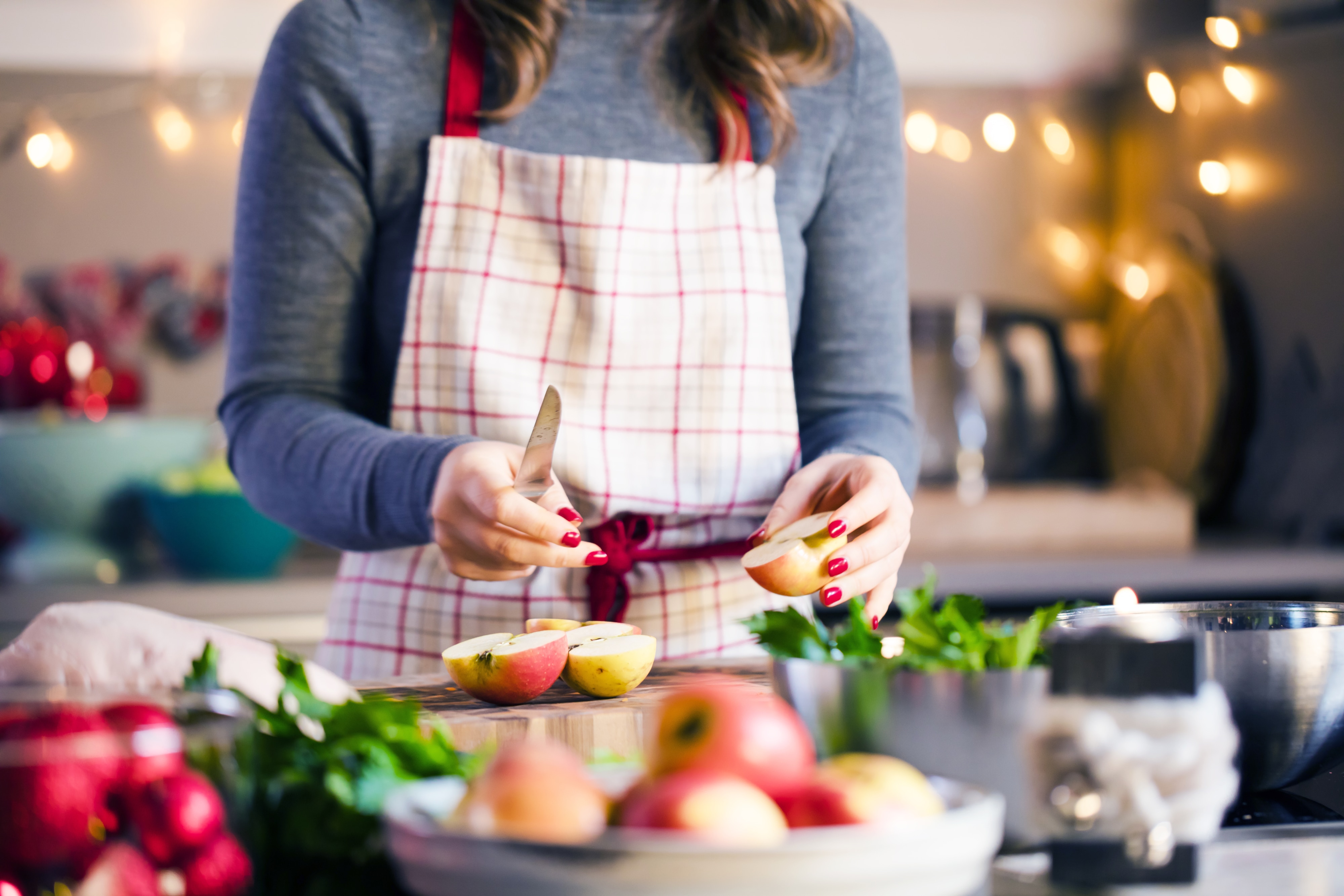 young woman in an apron cooking healthy food in the kitchen with holiday lights in the background